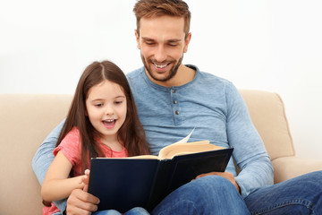 Father and daughter reading book on couch