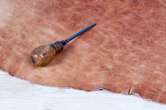Leather craft tools on a wooden background. Leather craftmans work desk . Piece of hide and working handmade tools on a work table