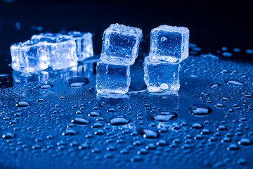 Wet ice cubes and water drop on blue background.