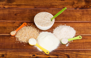 Bowl oatmeal, heap different cereals, measuring spoon against dark wood