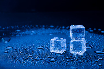 Wet ice cubes and water drop on blue background.