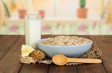 Bowl oatmeal, aglass milk, spoon and rose against kitchen.