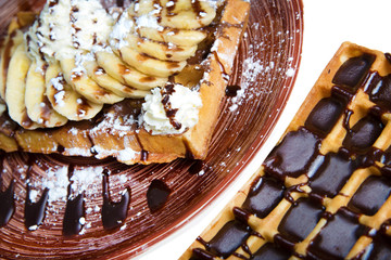 Plate of belgian waffles with cream, bananas and chocolate