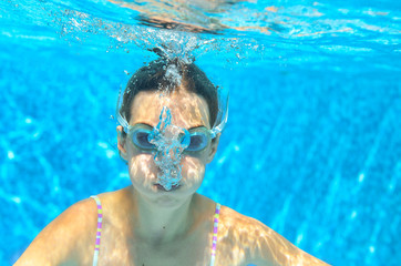 Naklejka premium Child swims in pool underwater, funny happy girl in goggles has fun under water and makes bubbles, kid sport on family vacation 