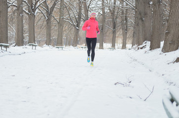 Winter running in park: happy woman runner jogging in snow, outdoor sport and fitness concept
