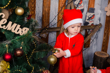 Happy little baby in Santa's costume near Xmas tree