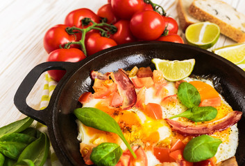 Pan of fried eggs with tomatoes, bacon, spinach, lime