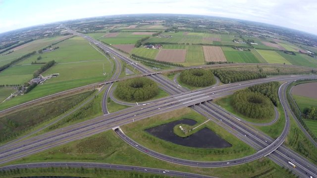 Aerial highway intersection cloverleaf flying away backwards high altitude moving away from clover showing traffic moving over road located within green grass landscape flat land 4k high resolution