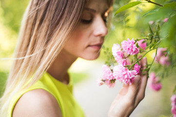 Naklejka premium Beautiful blond woman smelling pink rose flowers. Sunny summer.
