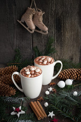 Two cups of hot cocoa or hot chocolate with christmas tree branches, old fashioned skates, cinnamon...
