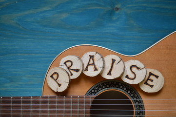 guitar on teal wooden background with wood pieces on it lettering the word: PRAISE