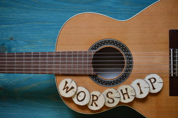 guitar on teal wooden background with wood pieces on it lettering the word: WORSHIP