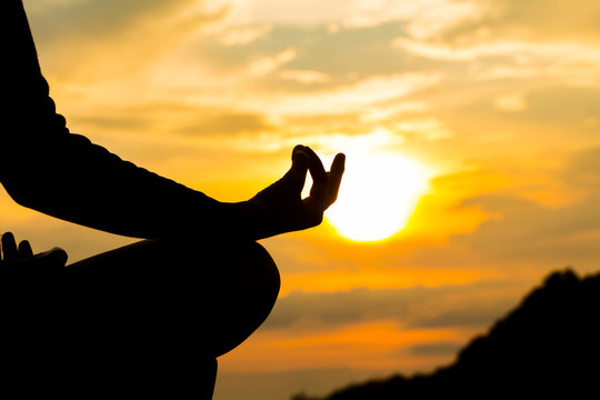 Silhouette, hand of Woman Meditating in Yoga pose or Lotus Position by the Sea at Sunset. Rear View. Nature Meditation Concept. Low key photo. relax time.