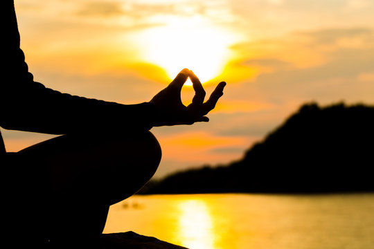 Silhouette, hand of Woman Meditating in Yoga pose or Lotus Position by the Sea at Sunset. Rear View. Nature Meditation Concept. Low key photo. relax time.