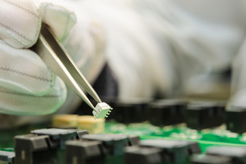 Fototapeta premium Female hand in ESD gloves holding tweezers and assembling white microchip on printed circuit board