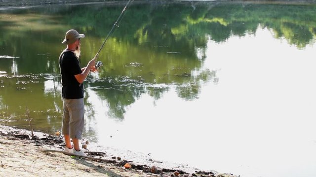 Sports fisherman fishing at lake using spinning rod and wheel, and casting technique