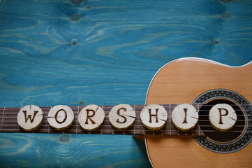 guitar on teal wooden background with wood pieces on it lettering the word: WORSHIP