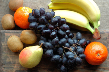 Lots of juicy fruit on a wooden surface: bananas, grapes, tangerines, kiwi, pears.