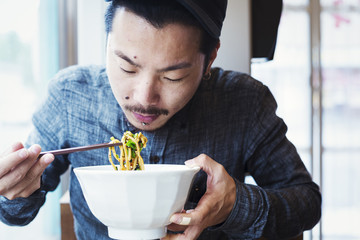 A ramen noodle cafe in a city.  A man seated eating ramen noodles from a large broth bowl. 