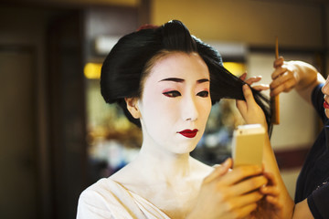 A modern geisha or maiko woman being prepared in traditional fashion, with white face makeup.
