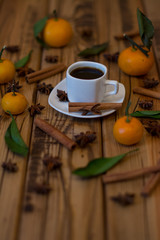 Small white cup of coffee, cinnamon sticks, star anise and mandarins on wooden background