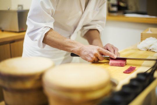A chef working in a small commercial kitchen, an itamae or master chef slicing fish with a large knife for making sushi