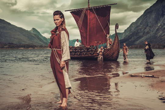 Viking woman standing near Drakkar on seashore