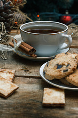 Beautiful concept. Chocolate cookies on a white plate on a wooden background and tea. Nearby stands a Christmas tree, toys, garlands and Christmas toys.