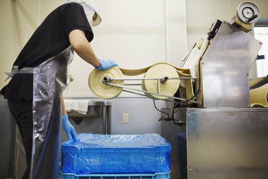 A Soba noodle factory.  Sheets of fresh noodle dough being passed through a large pressing machine. 