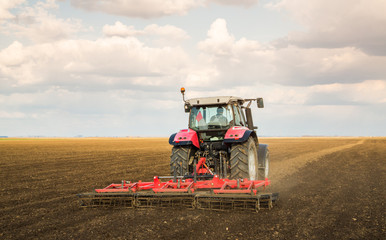 Obraz premium Farmer in tractor preparing land with seedbed cultivator