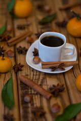 Small white cup of coffee, cinnamon sticks, star anise, hazelnuts and mandarins on wooden background