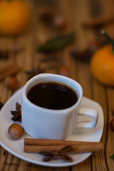 Small white cup of coffee, cinnamon sticks, star anise, hazelnuts and mandarins on wooden background
