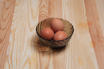 Three boiled eggs in a shell in a plate on a wooden table. Ingredients for a dish herring under a fur coat.