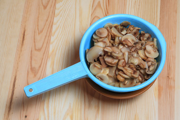 The frozen cut champignon mushrooms in a blue colander on a wooden table. Ingredients for French-style meat.