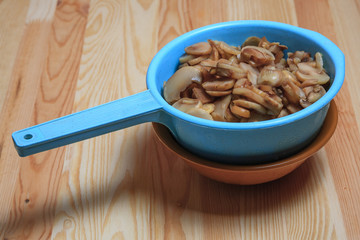 The frozen cut champignon mushrooms in a blue colander on a wooden table. Ingredients for French-style meat.
