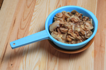 The frozen cut champignon mushrooms in a blue colander on a wooden table. Ingredients for French-style meat.