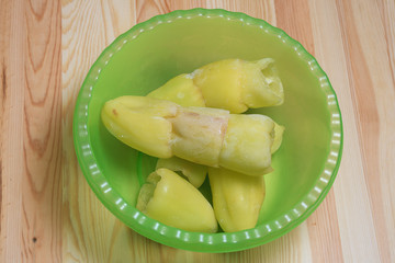  The frozen sweet pepper in a soup green plastic plate on a wooden table. Ingredients for stuffed peppers.