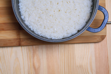 Boiled rice in a dark blue pan on a wooden table. Ingredients for stuffed peppers. 