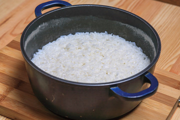 Boiled rice in a dark blue pan on a wooden table. Ingredients for stuffed peppers. 