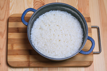 Boiled rice in a dark blue pan on a wooden table. Ingredients for stuffed peppers. 