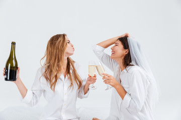 Two smiling women wearing bridal veil and holding champagne bottle