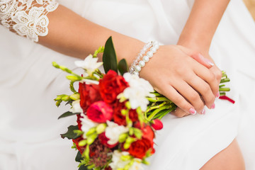 Obraz na płótnie Canvas Close up of bridal wedding bouquet of roses in hands of young bride. Woman dressed in white dress wearing bracelet of pearls on wrist. Fingers with classic french pink and white nails manicure