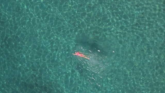 AERIAL: Active girl swimming backstroke technique in amazing crystal clear ocean