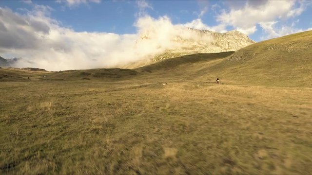 Aerial shot of mountain biker riding the trail on alpine pass in autumn season


