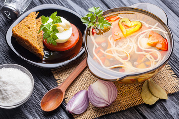 Fototapeta na wymiar Fresh vegetable soup with noodles in a pot on black