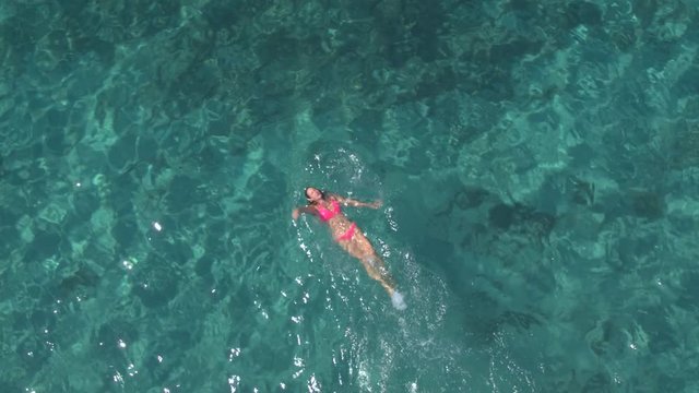 AERIAL: Attractive girl swimming backstroke in amazing crystal clear ocean water
