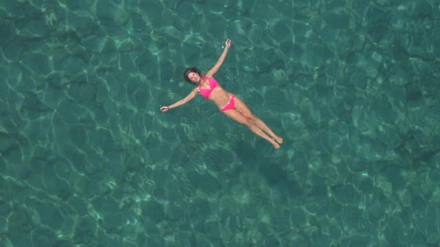 AERIAL: Pretty young woman swimming starfish float in crystal clear ocean lagoon