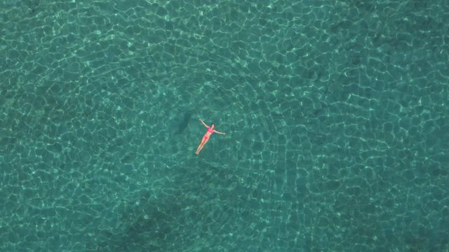 AERIAL: Beautiful young woman swimming starfish float in crystal clear ocean