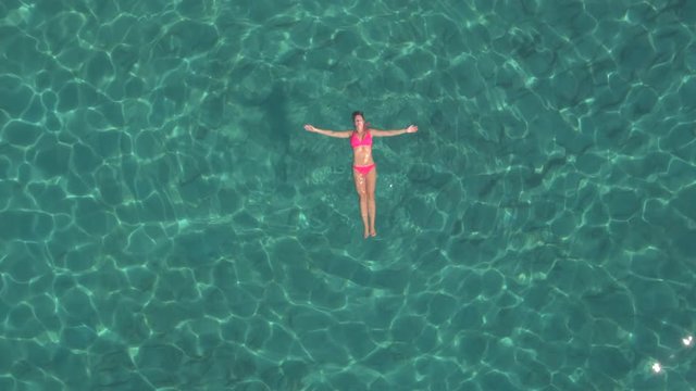 AERIAL: Attractive young woman swimming starfish float in crystal clear ocean