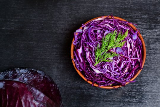Shredded red cabbage in clay bowl on black background. Vegetarian healthy food. Top view